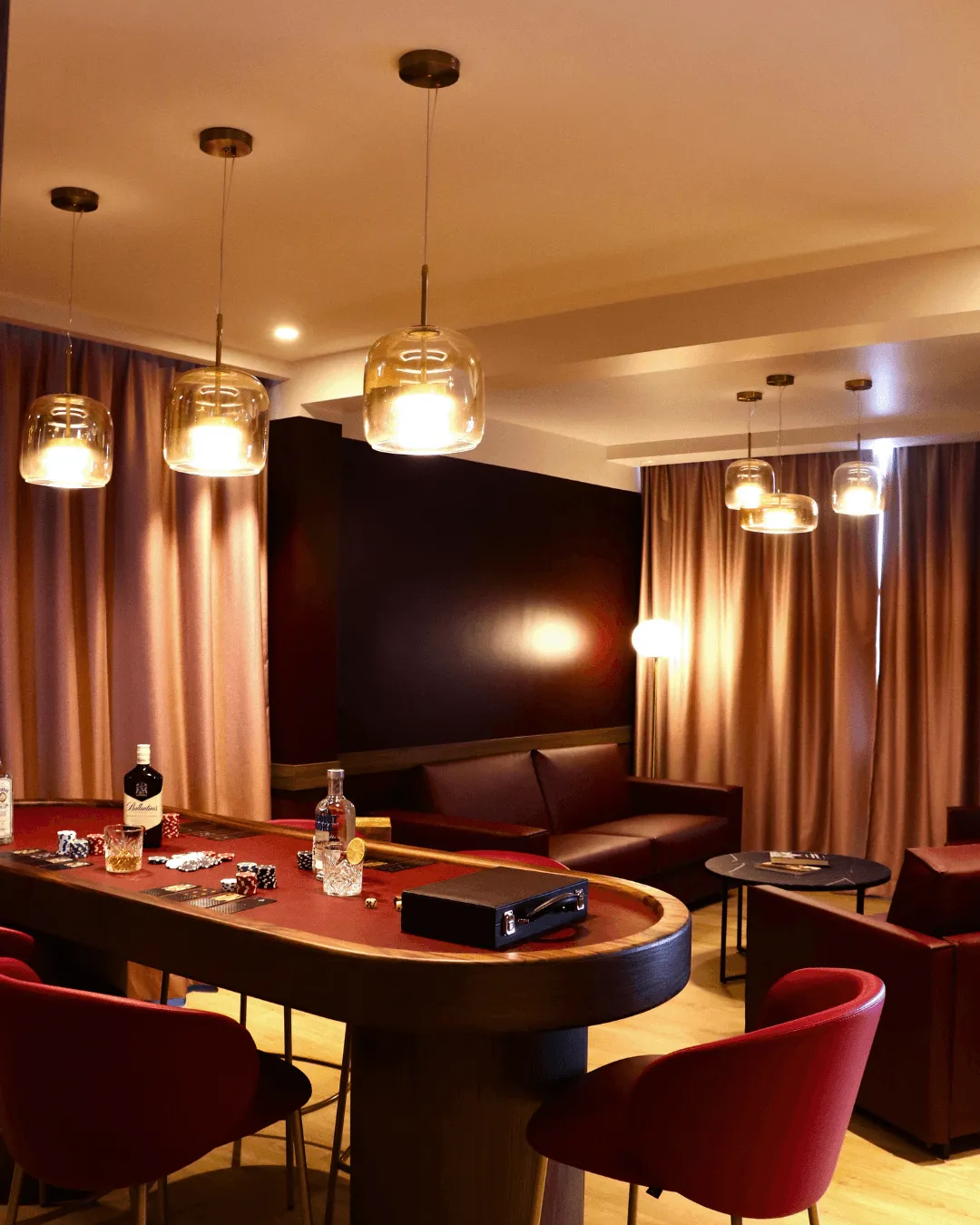 Spielzimmer mit Pokertisch, roten Stühlen, Hängeleuchten und braunen Ledersofas