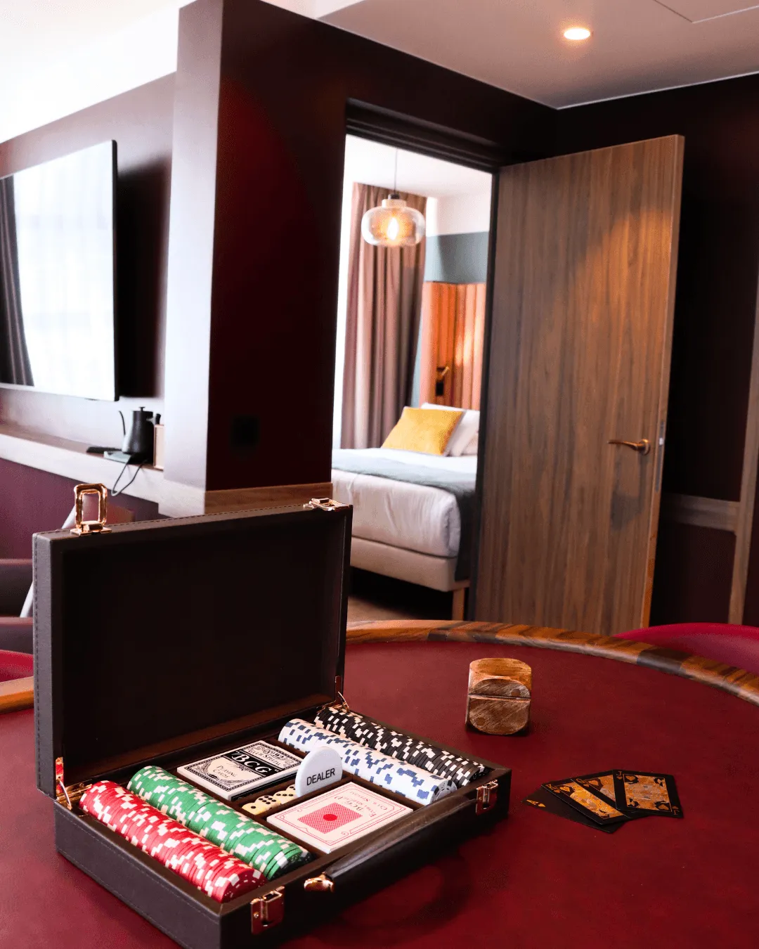 Ein Spieltisch mit einem offenen Kasten, der Chips, Karten und einen "DEALER"-Chip enthält, in einem Hotelzimmer mit einem im Hintergrund sichtbaren Bett