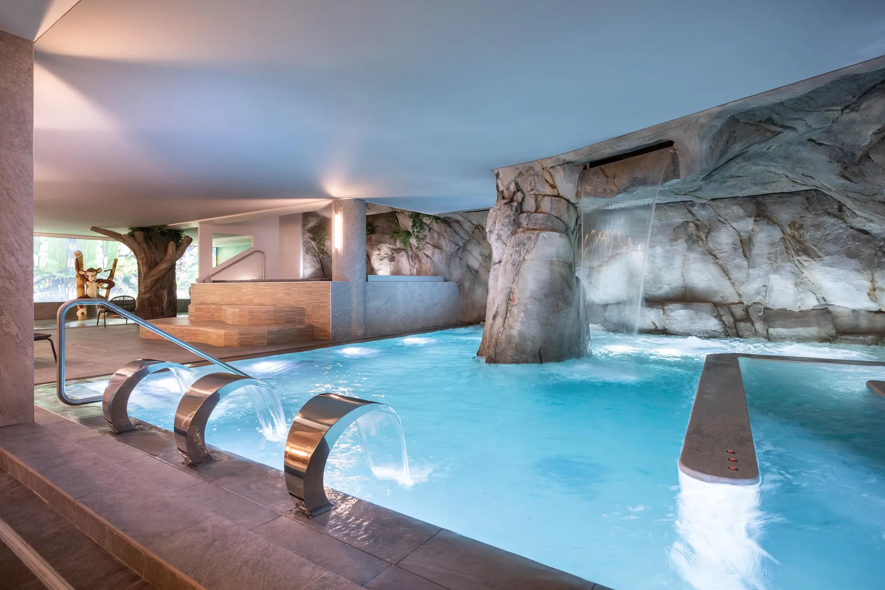 Indoor pool with waterfalls and artificial rocks, lit by soft natural light