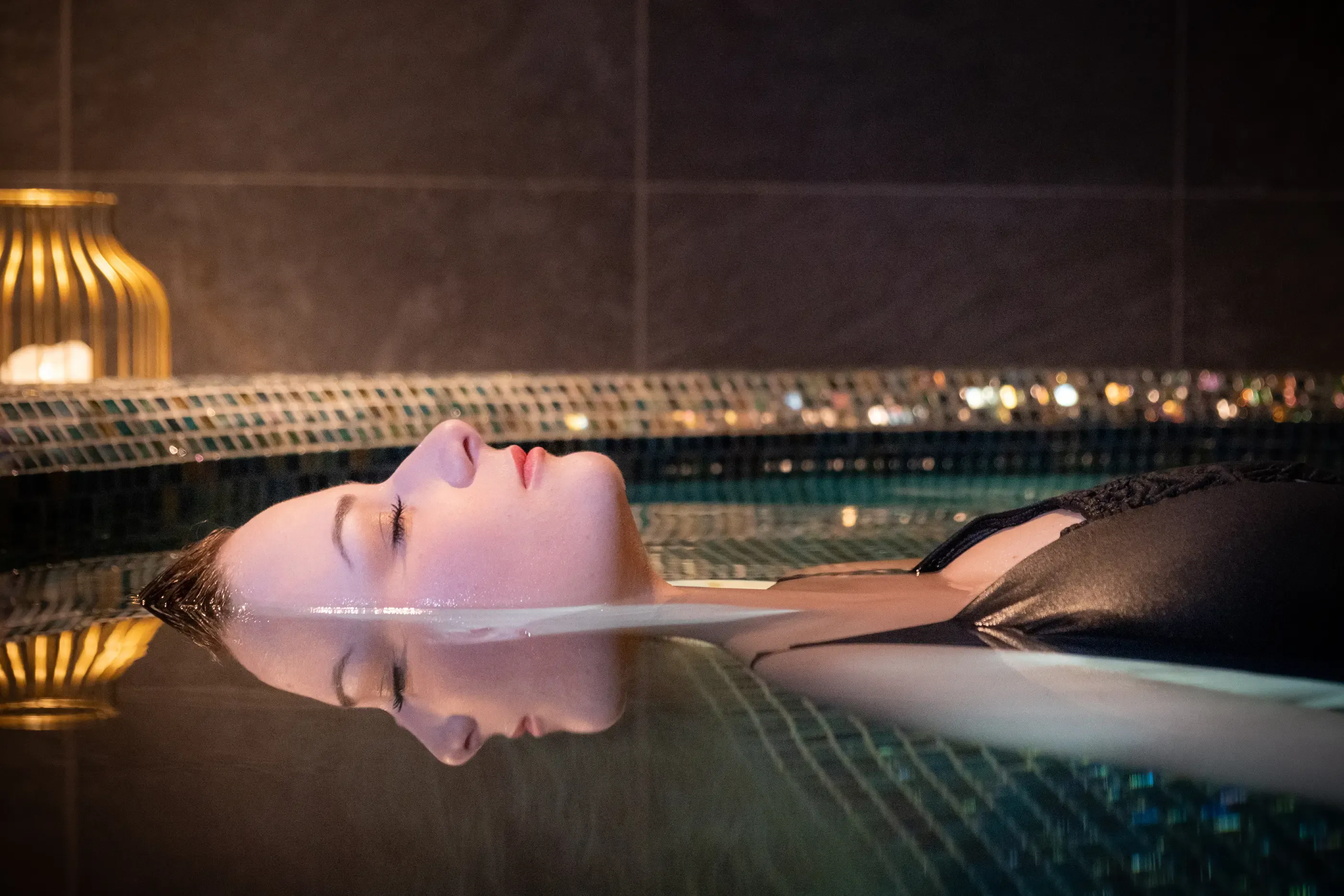 Une personne allongée sur le dos dans une piscine avec une vue nocturne floue en arrière-plan