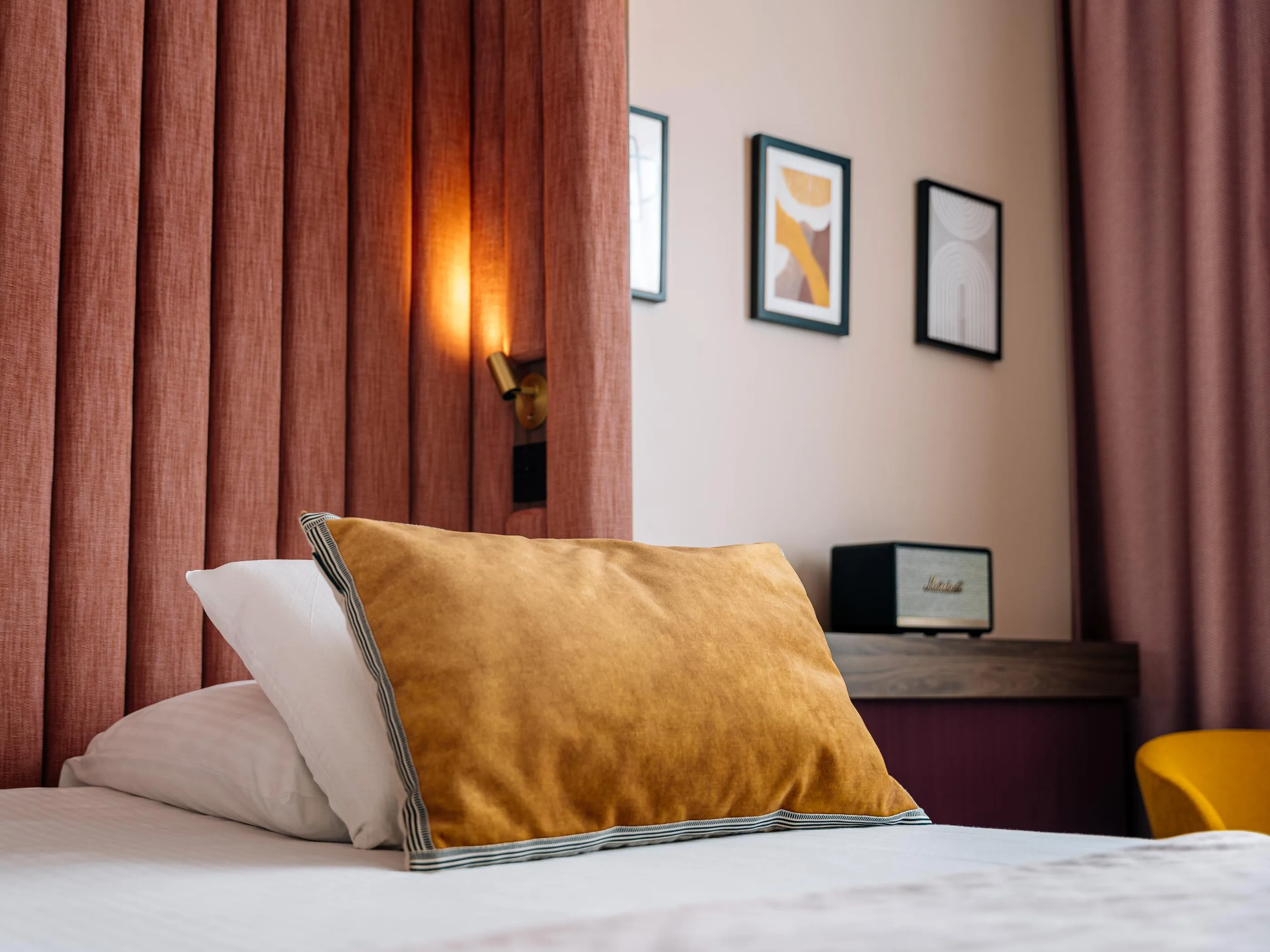 Bett mit Kissen, eine Lampe an und Bilder an der Wand