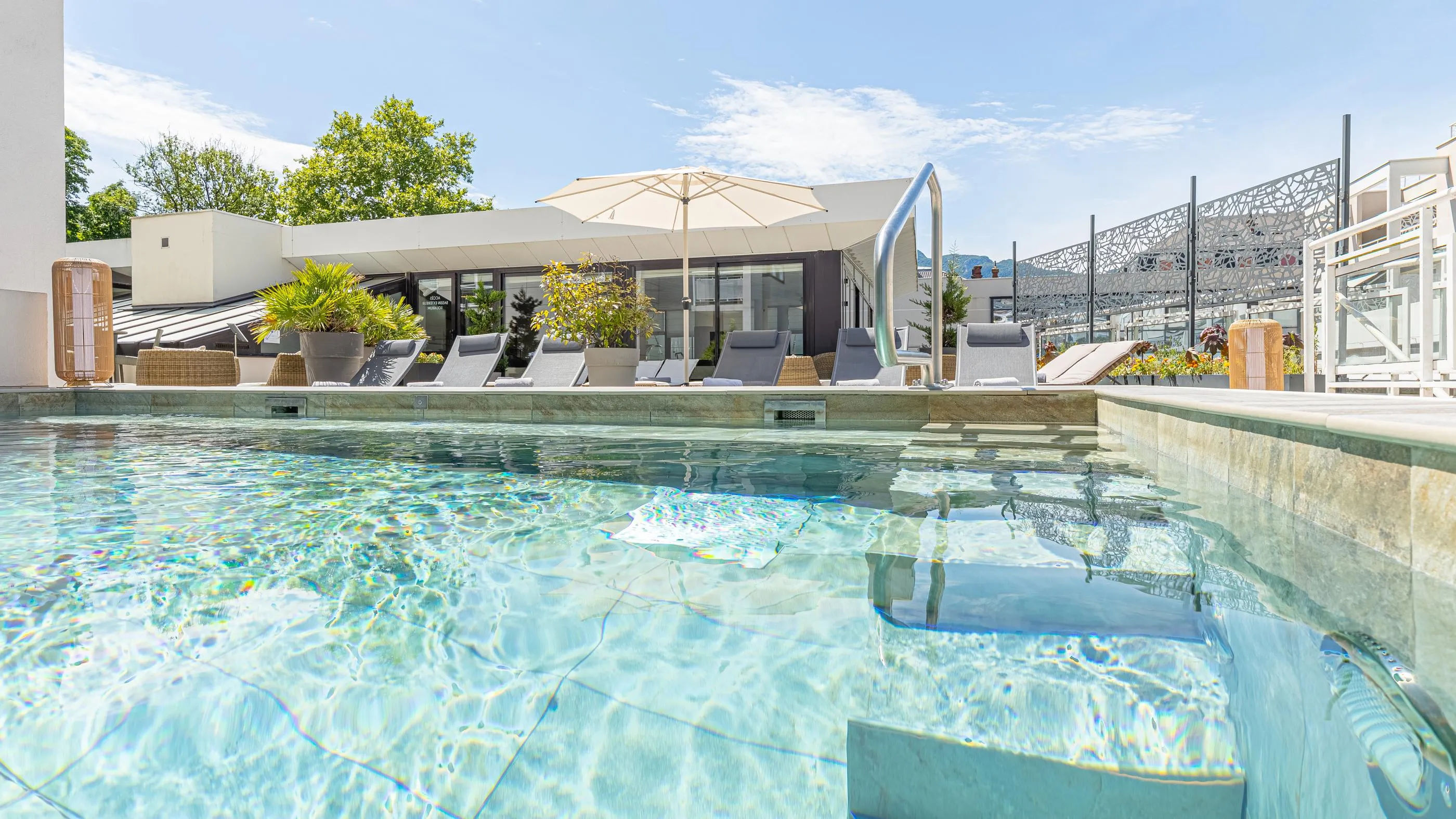 Schwimmbad mit Blick auf eine Terrasse mit Liegestühlen, Sonnenschirmen und Pflanzen