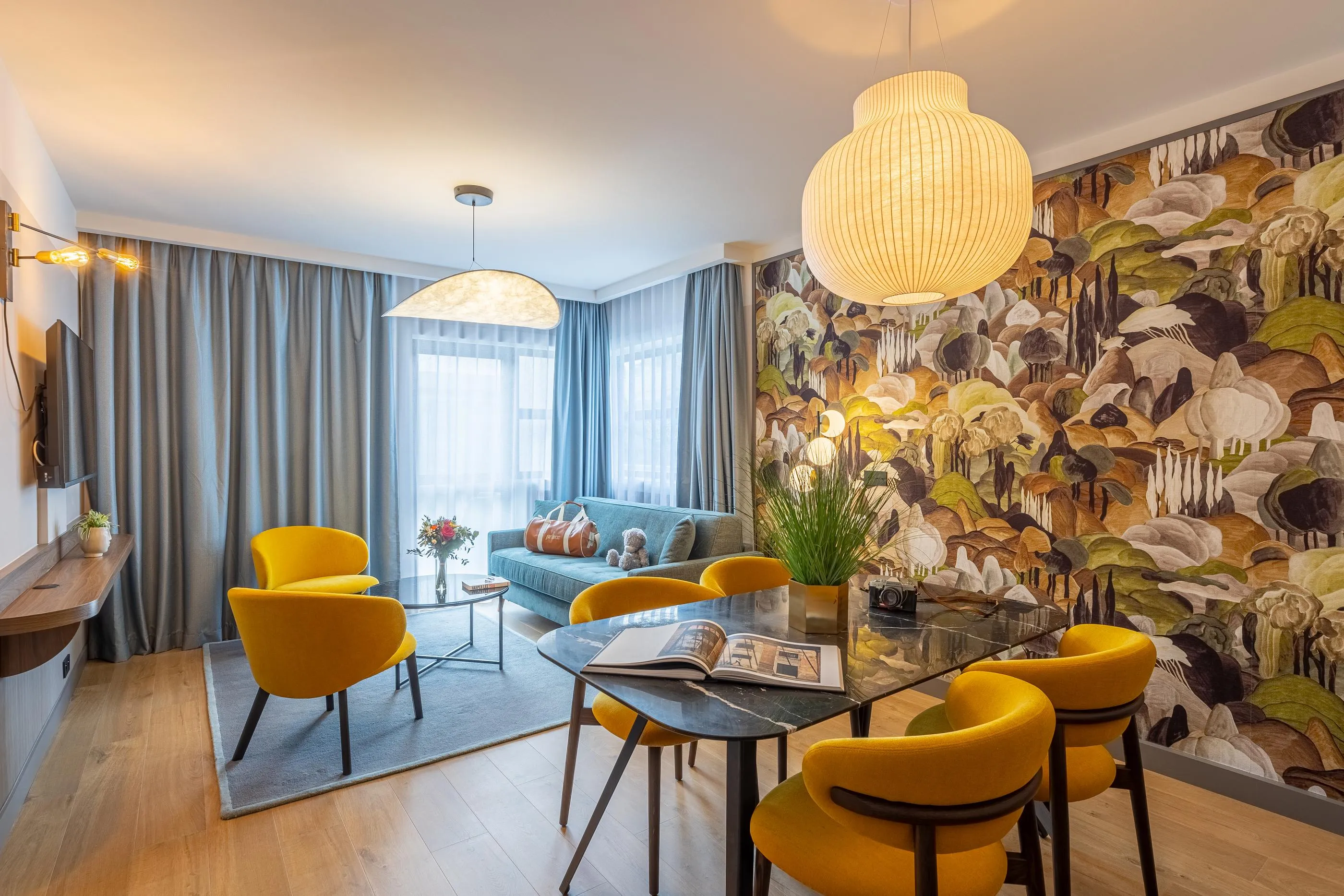Moderner Salon mit blauem Sofa, gelben Stühlen, Glastisch und mit floralen und pilzförmigen Mustern verzierter Wand