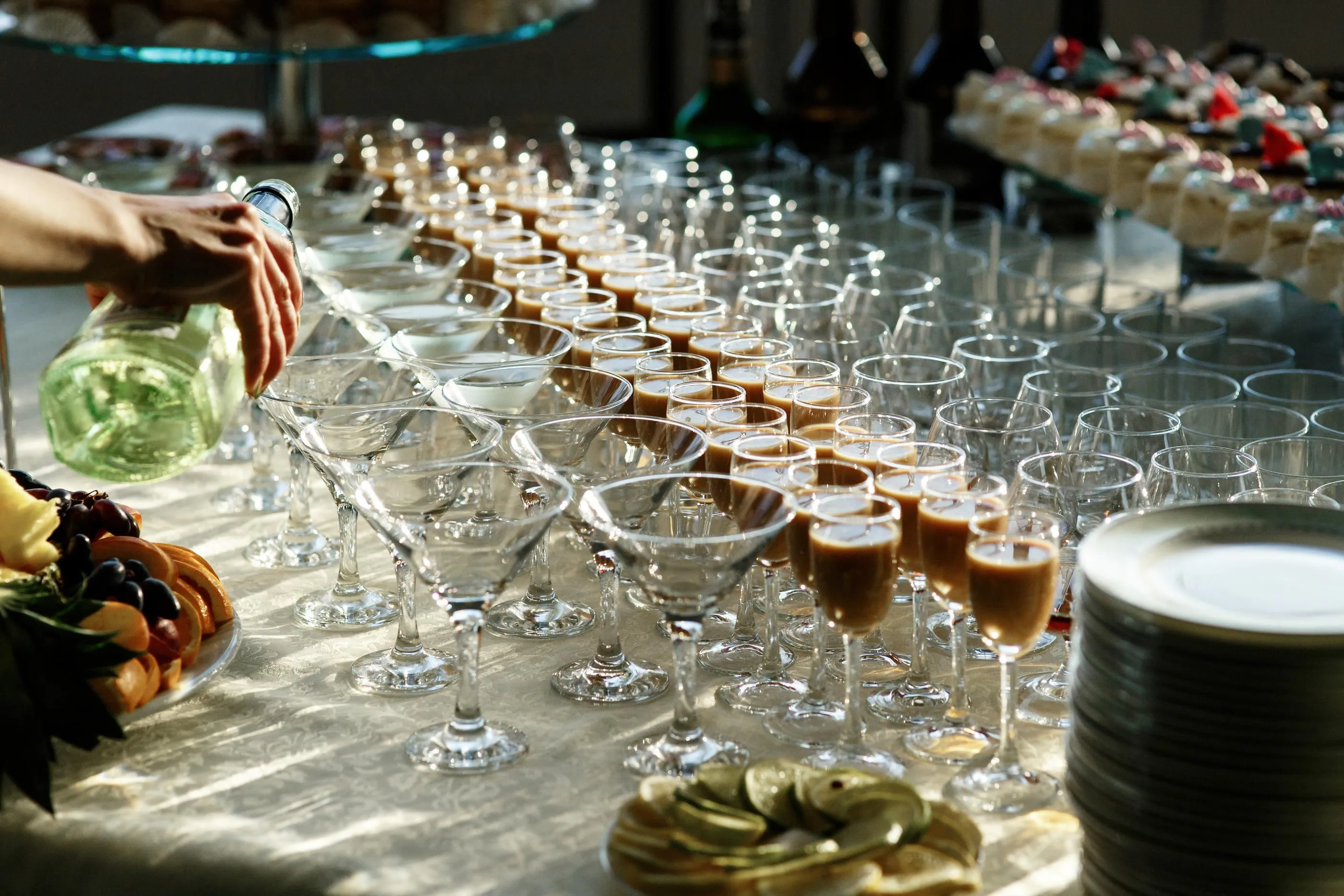 Une personne verse un liquide dans des verres à cocktail disposés sur une table, entourés de plateaux de nourriture